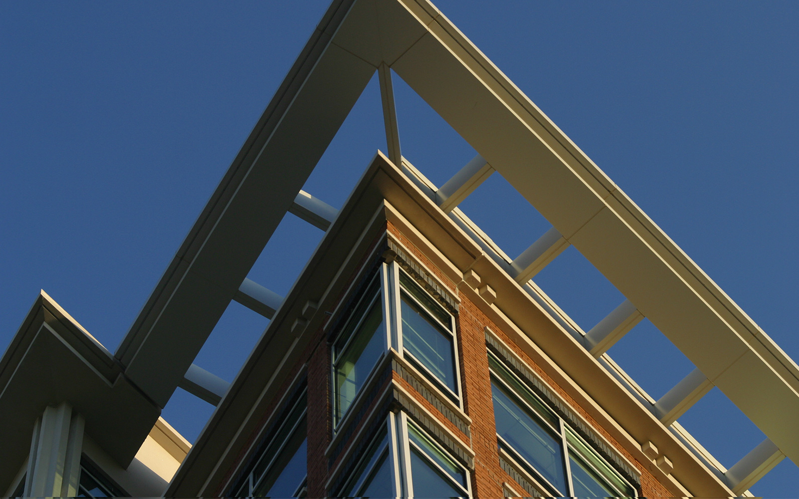 The top corner of a modern building, as seen from below, with blue sky in the background
