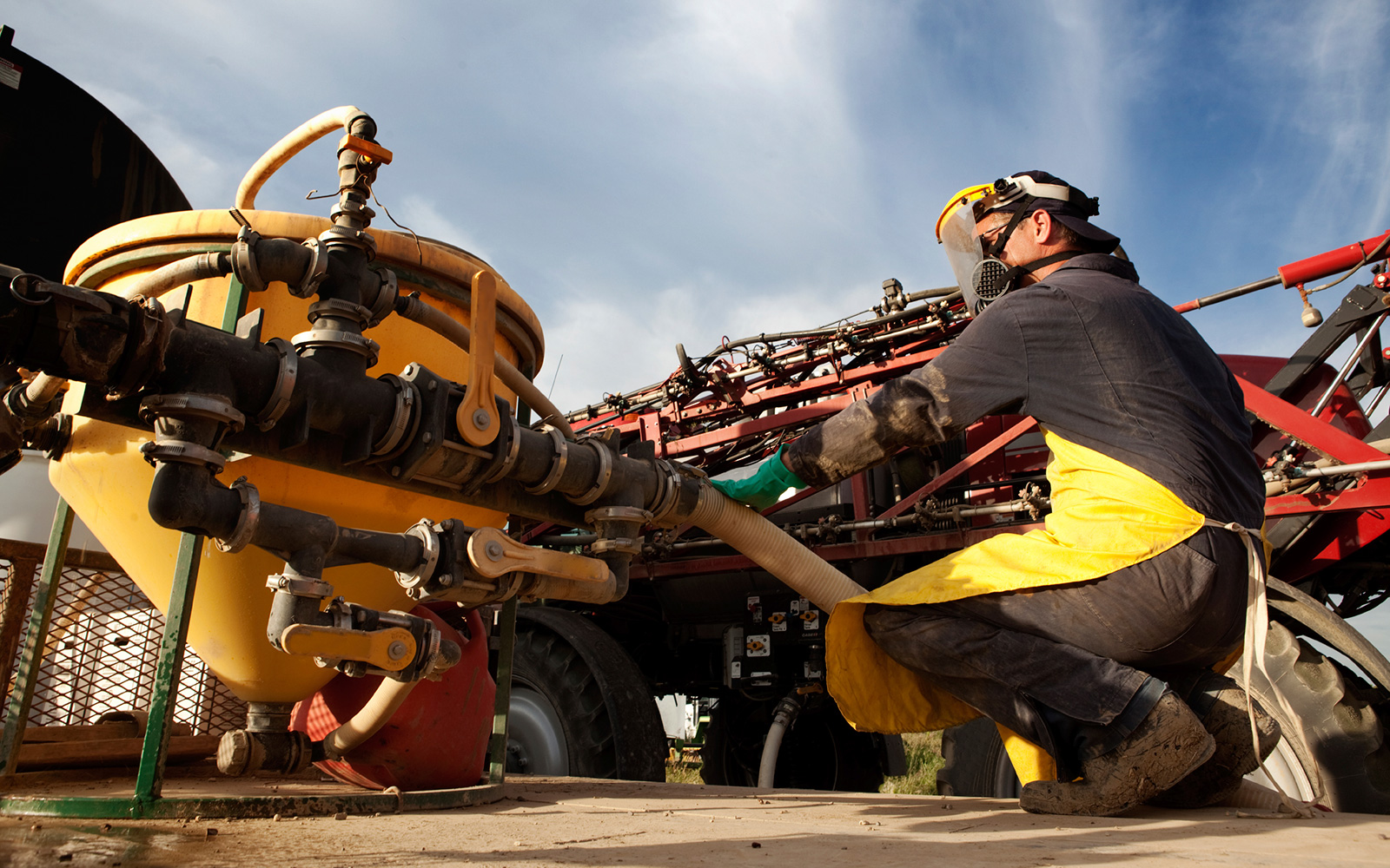 Worker wearing a gas mask and visor inspects machinery in an industrial setting