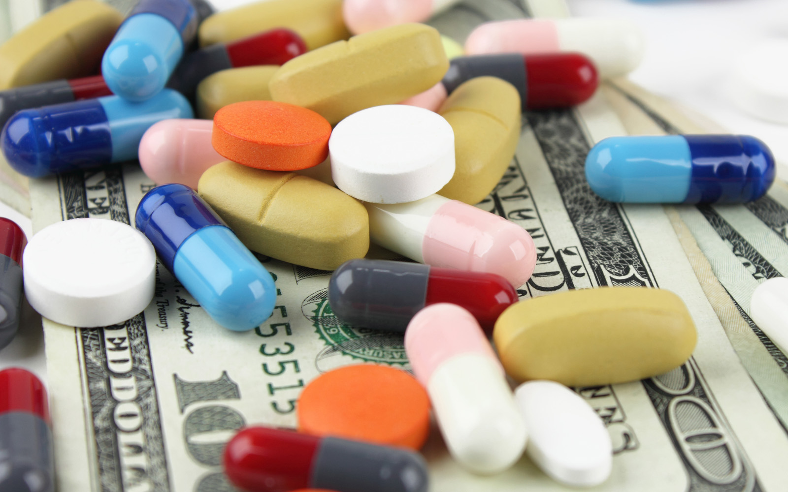 a variety of prescription medication pills lying on top of dollar bills