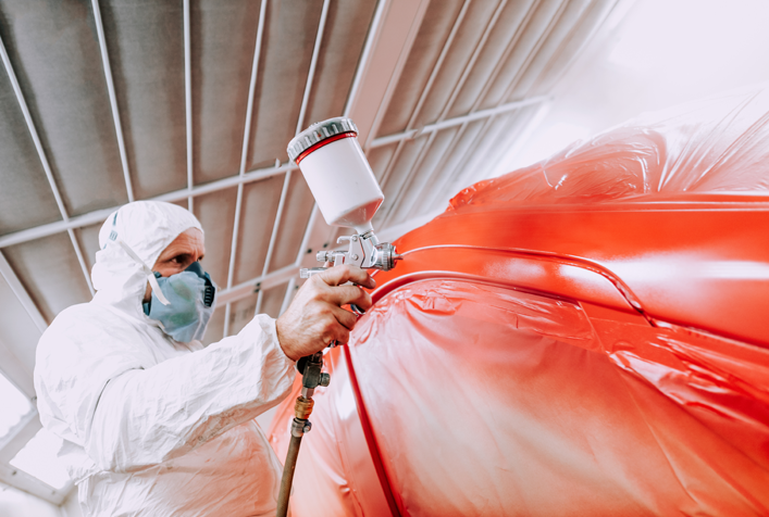 Photo of a worker in protective gear using a paint sprayer on an automobile