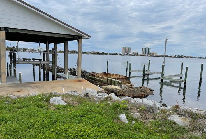 photo of posts left over from a boat dock and a housing to hold a boat on the water. city buildings off in the background