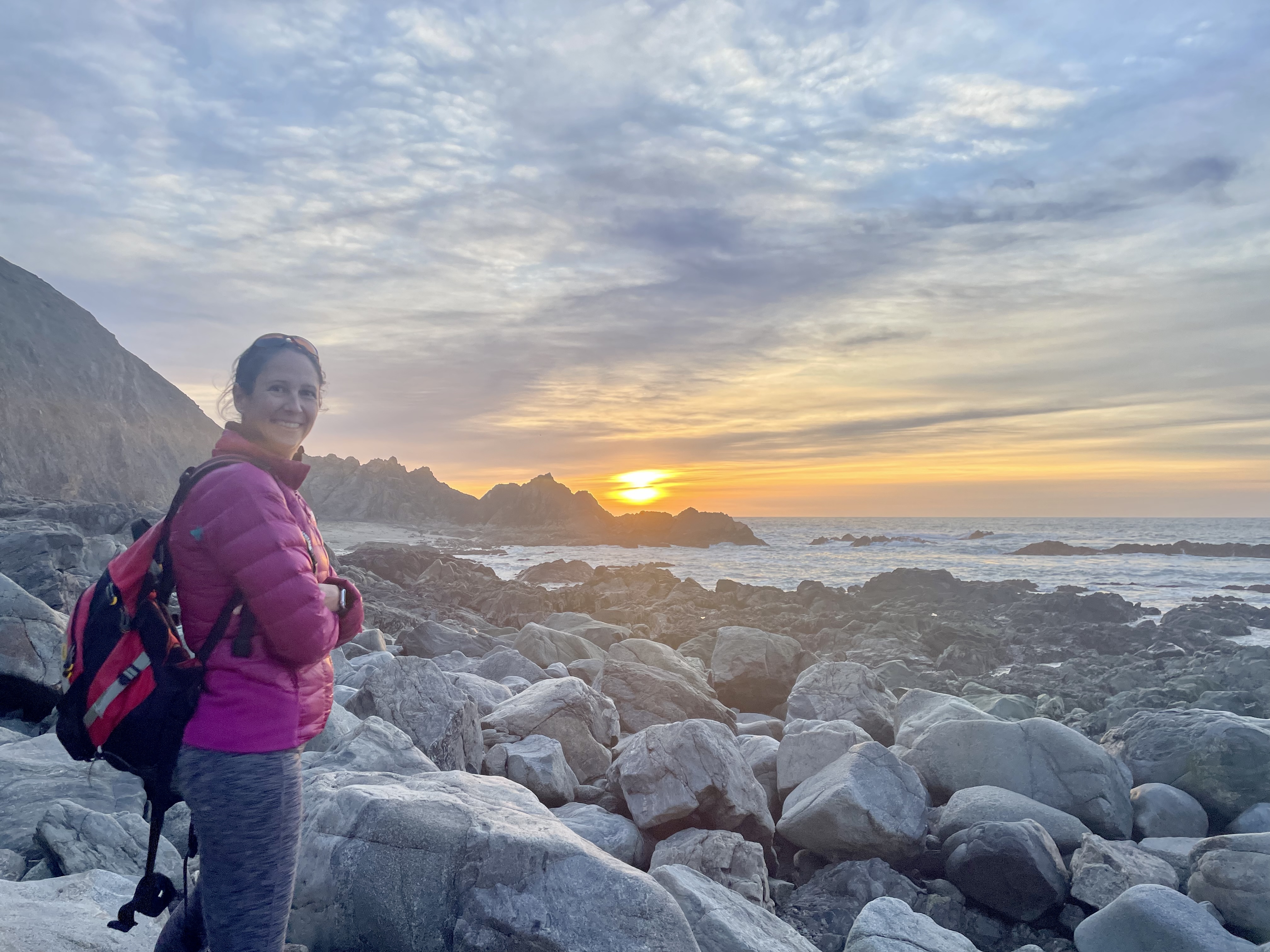 A woman stands on a rocky beach at sunset