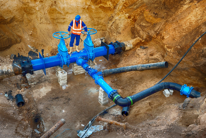 photo of a large, deep, ditch with a person standing on large water piping with shut off valves