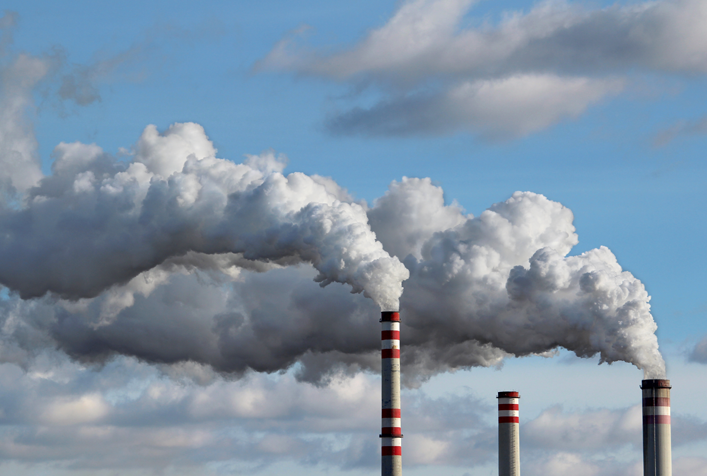 Image of the top of 3 smoke stacks with white smoke polluting the skyline