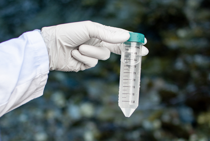 gloved hand holding a water sample in a measuring tube
