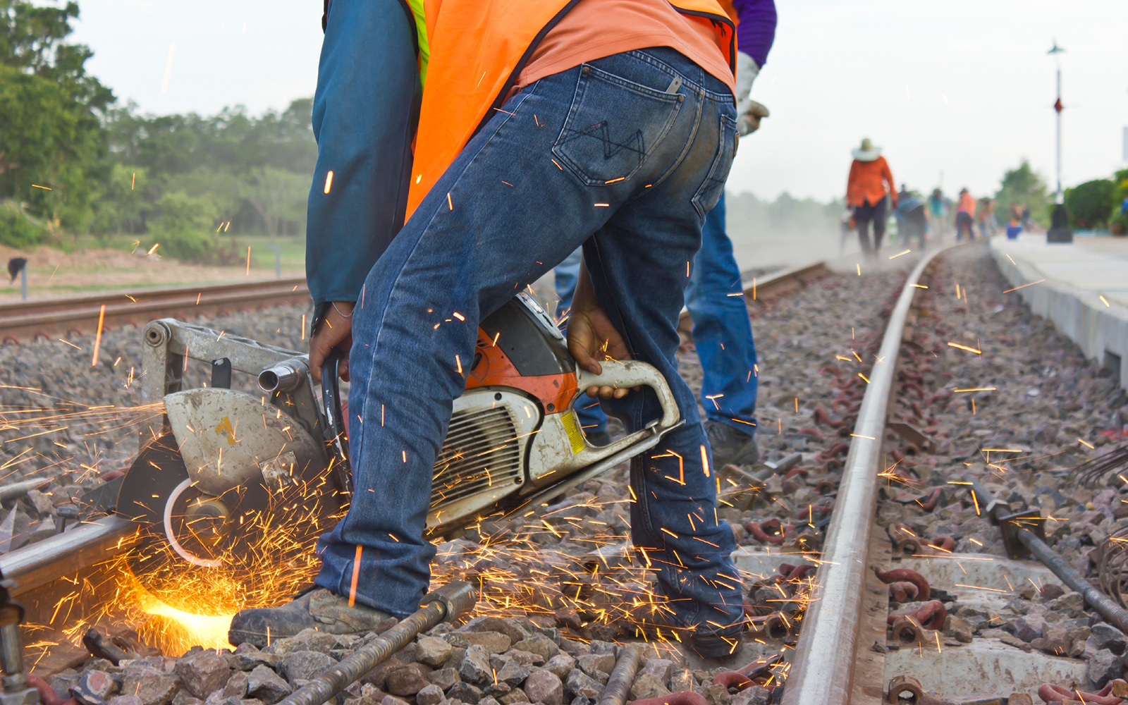 Sparks fly from a circular saw operated by a worker cutting a rail on a railway