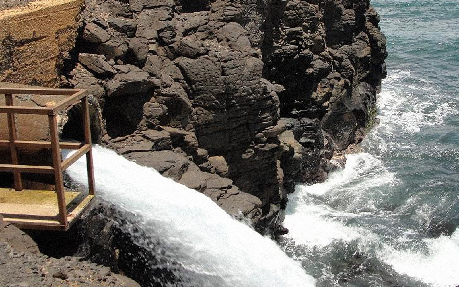 Along the coast, water flows from a pipe into ocean water breaking against a natural rockwall