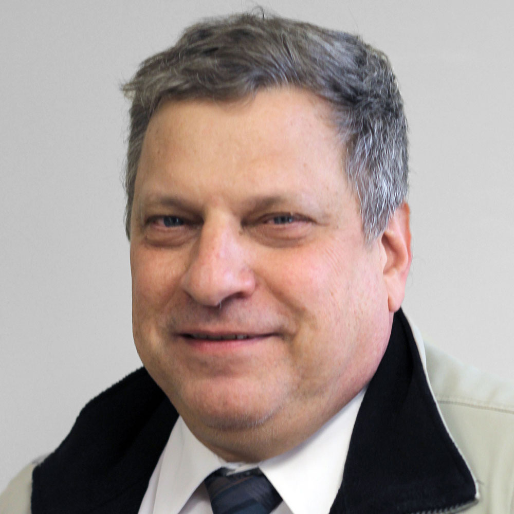 Man in a tan jacket, white shirt, and black tie