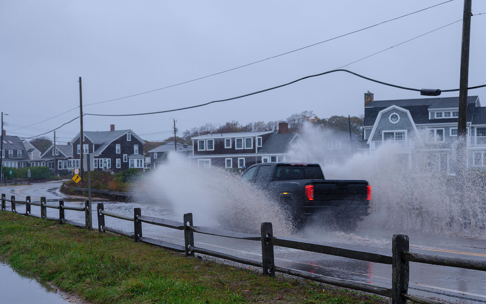 A truck drives through a large puddle on a road in a residential area