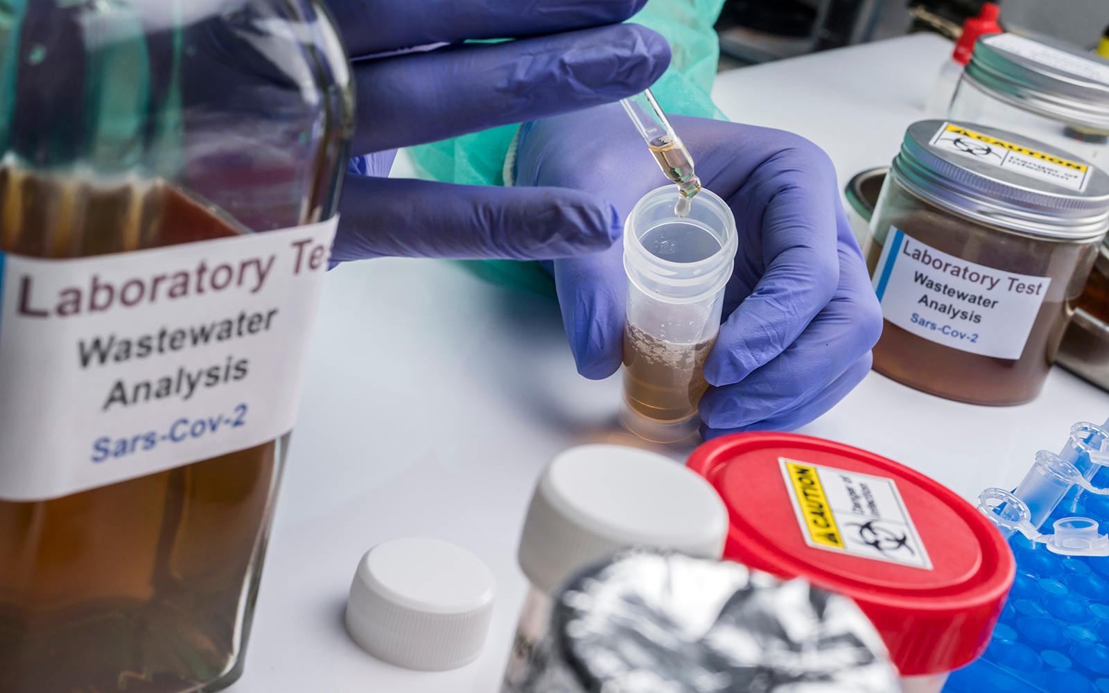 A gloved hand holding a dropper picks up COVID-19 wastewater samples in a labortory.