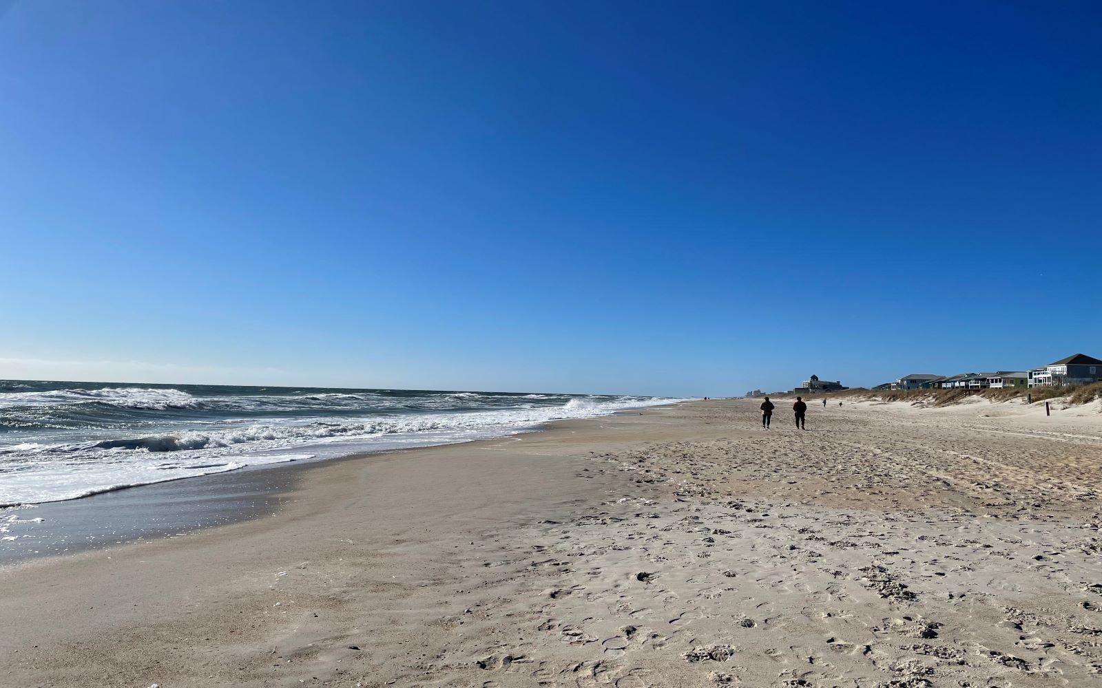 a wide beach during the afternoon with a few people walking on it.