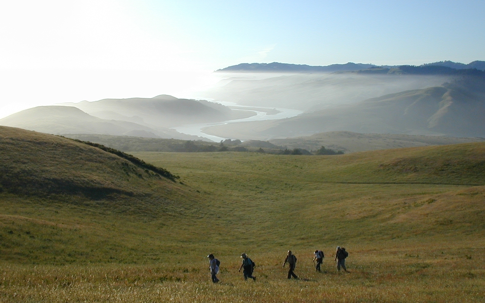 people walking in a valley with a river and hills in the background