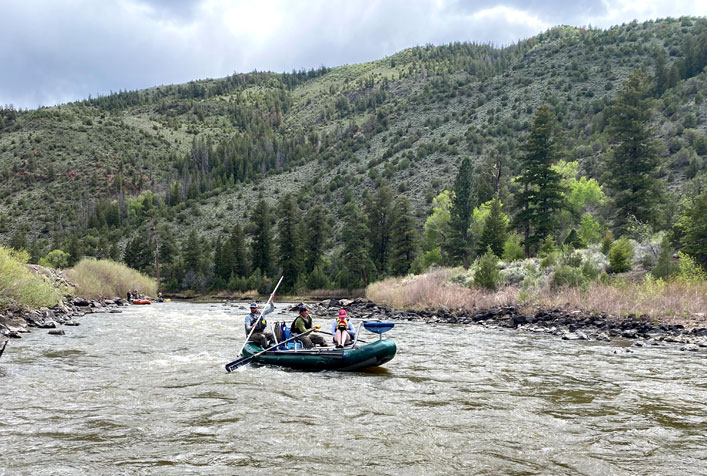 photo of people padding on a river at the base of tree covered mountain