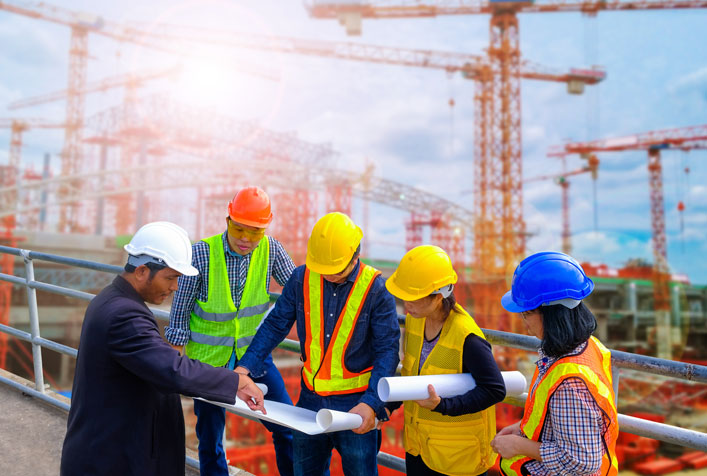 Photo of construction executives with hard hats and bright safety vests looking a blueprints