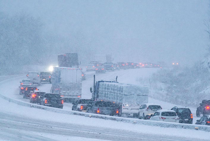 photo of a line of cars and trucks in heavy traffic along a highway during a winter storm