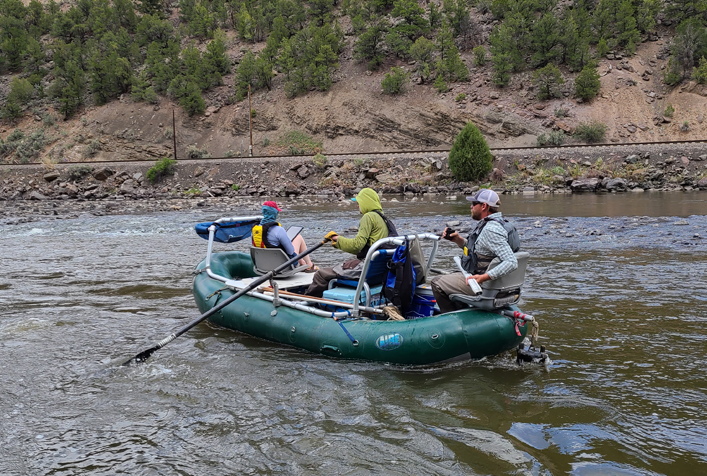 photo of 3 people in a raft on a river who appear to be making assessments and recording data.