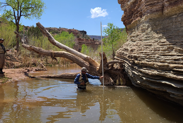 person standing waist deep in water taking depth measurements
