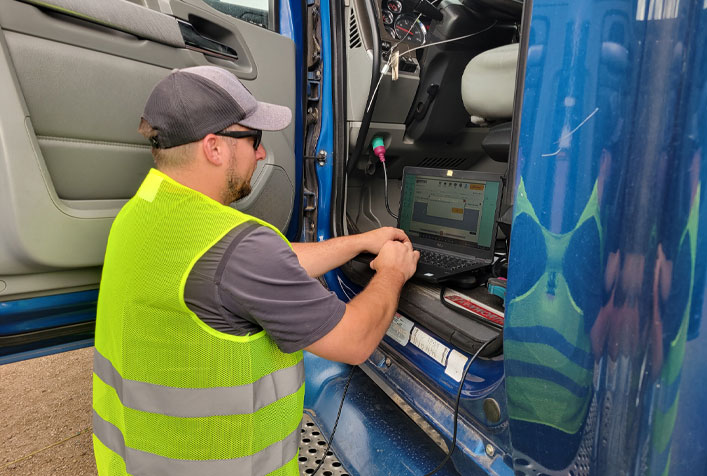 Photo of person with safety vest kneeling next to a vehicle conducting diagnostics