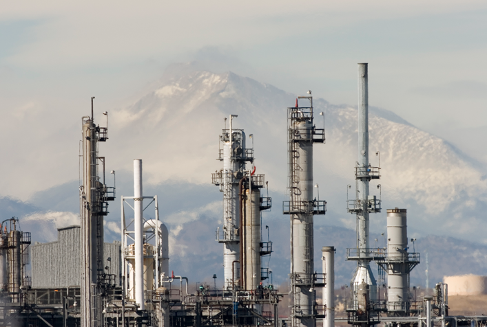 photo of a petroleum refinery showng the tall stacks with mountains in the distance