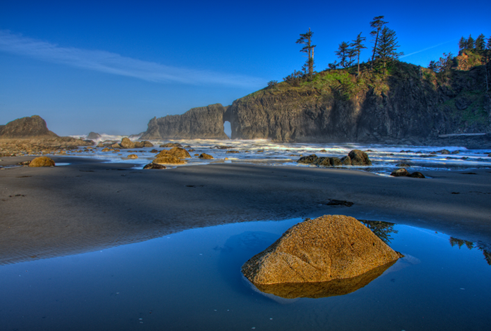 photo of sandy coast with scattered boulders an oceanside cliffs in the distance