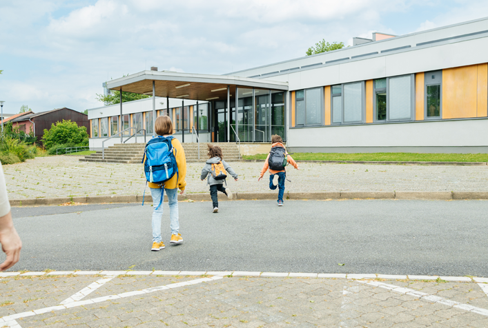 Photo of 3 children with backpacks heading in to the front doors of school