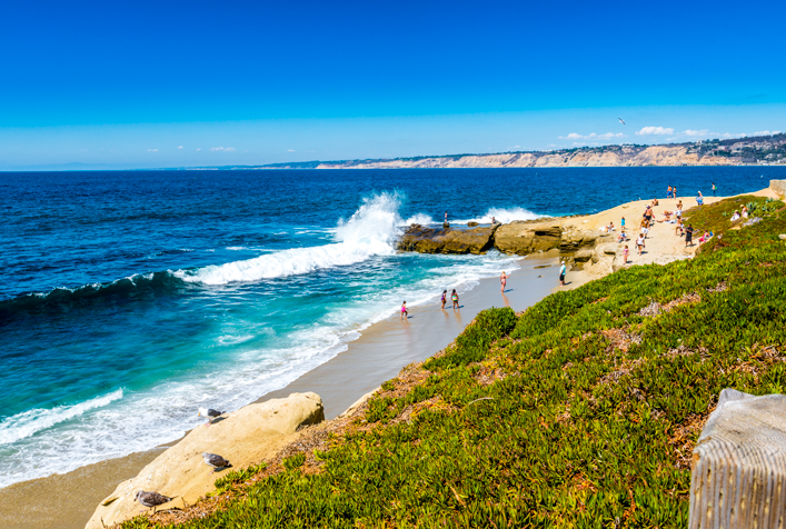 photo showing a shoreline with crashing waves against rocks and people hanging out
