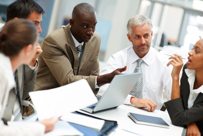 Photo of people collaborating while sitting around a laptop and documents