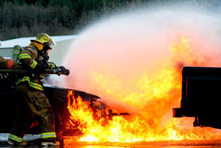 Image of firefighter hosing down flames rising from the ground
