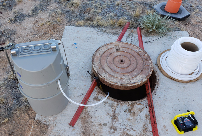 image of a well with a cover partially removed showing a tube placed down from a sampling unit