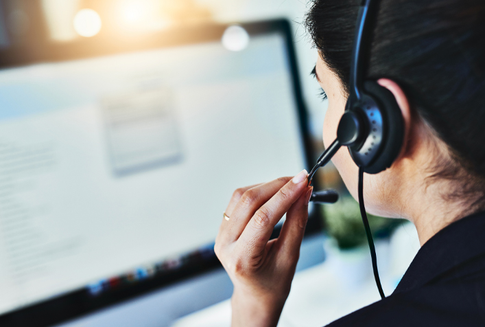 sideview image of a person with a telephone headset sitting in front of a computer screen