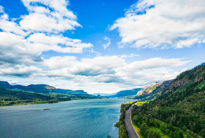 photo of the Columbia River basin with clouds in the sky and a highway running alongside the water