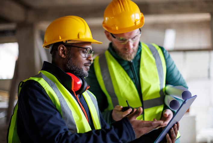 two workers in hard hats looking at a clipboard together inside a building