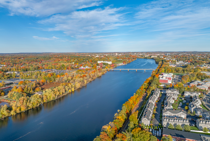 Aerial view of Massachusetts river and its banks, including buildings and trees in autumn foliage