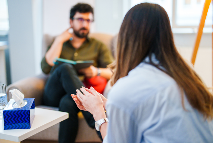 Photo of young woman talking to a man in what appears to be a therapy setting.