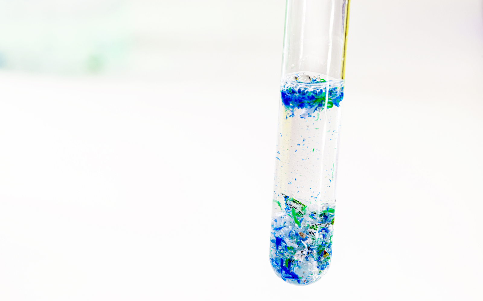Test tube filled with green, blue, and white microplastics